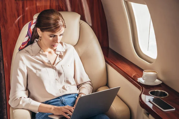 Mujer atractiva en camisa usando el ordenador portátil en avión privado - foto de stock