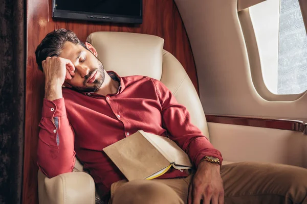 Красивий чоловік у сорочці спить з книгою в приватному літаку — стокове фото
