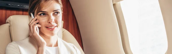 Tiro panorâmico de mulher de negócios sorridente em terno falando no smartphone no avião privado — Fotografia de Stock