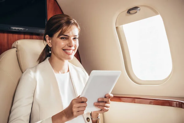 Smiling businesswoman in suit using digital tablet in private plane — Stock Photo