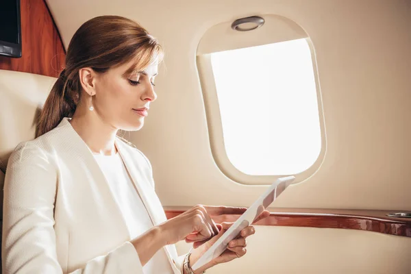 Attractive businesswoman in suit using digital tablet in private plane — Stock Photo