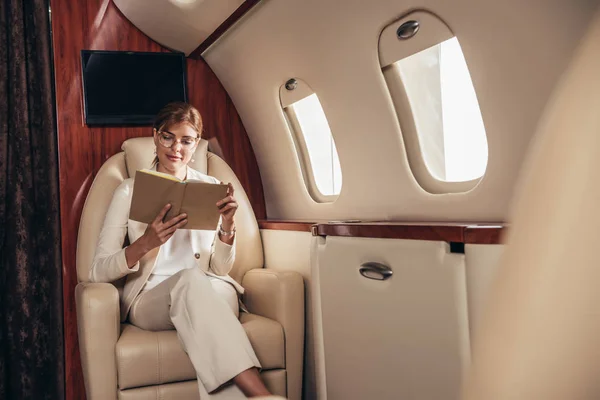 Attractive businesswoman in suit reading book in private plane — Stock Photo