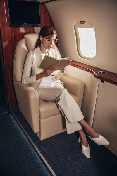 Mulher de negócios atraente no livro de leitura de terno no avião privado — Fotografia de Stock