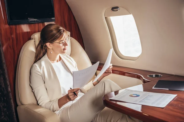 Atractiva mujer de negocios en traje haciendo papeleo en avión privado - foto de stock