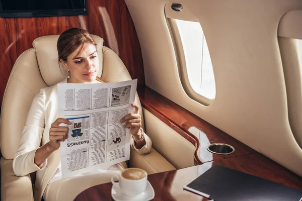Attractive businesswoman in suit reading newspaper in private plane — Stock Photo