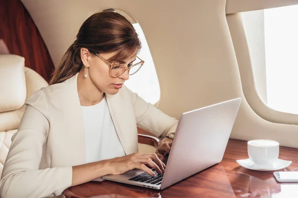 Attraente donna d'affari in giacca e cravatta utilizzando computer portatile in aereo privato — Foto stock