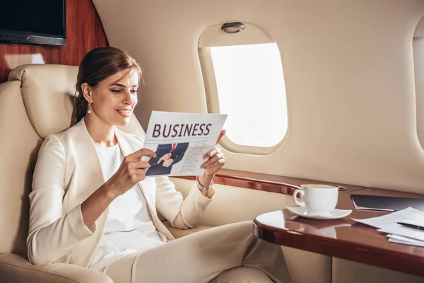 Smiling businesswoman in suit reading newspaper business in private plane — Stock Photo