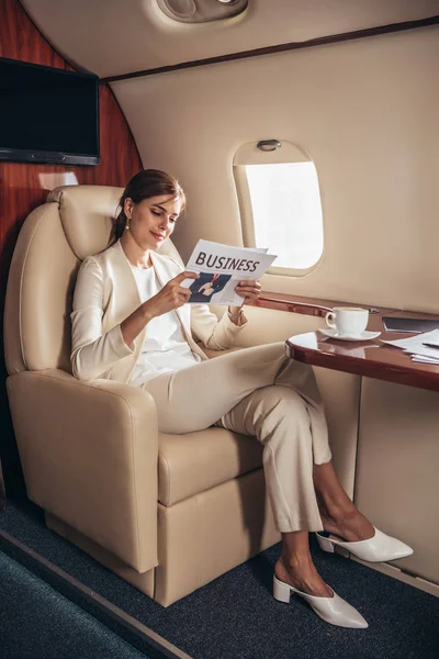 Femme d'affaires souriante en costume lecture affaires de journaux dans un avion privé — Photo de stock