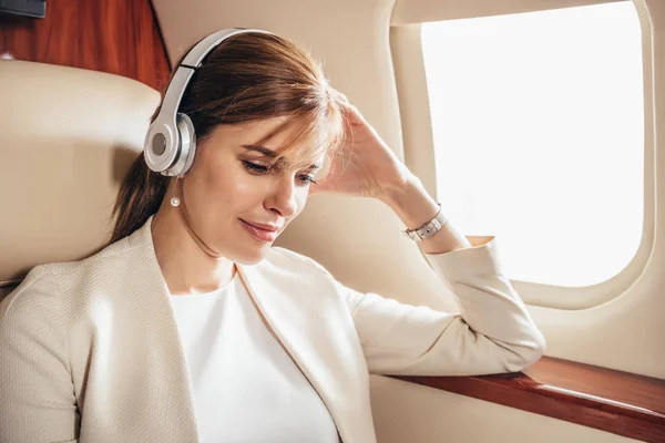Attractive businesswoman in suit listening music with headphones in private plane — Stock Photo