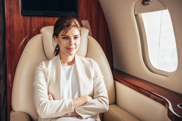 Attractive businesswoman in suit with crossed arms looking at camera in private plane — Stock Photo