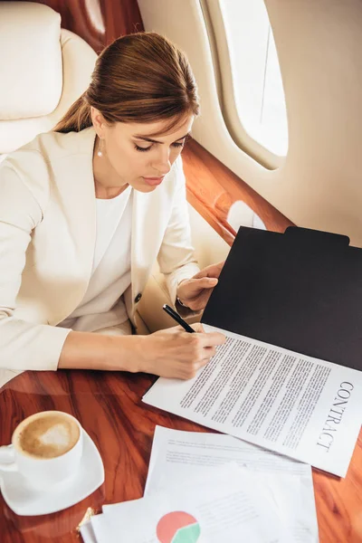 Vista de ángulo alto de atractiva mujer de negocios en traje firma contrato en avión privado - foto de stock