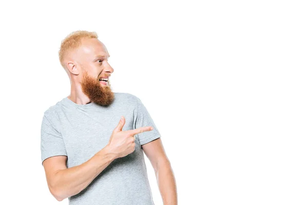 Красивый бородатый улыбающийся мужчина в серой футболке, указывающий изолированным на белом — стоковое фото