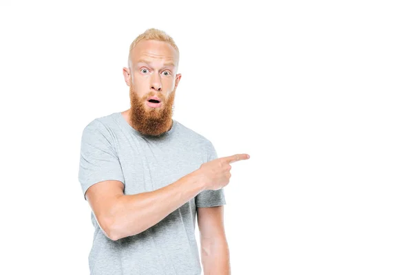 Guapo barbudo sorprendido hombre en gris camiseta apuntando aislado en blanco - foto de stock