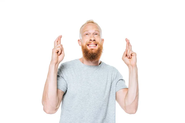 Handsome bearded man in grey t-shirt with fingers crossed looking up, isolated on white — Stock Photo