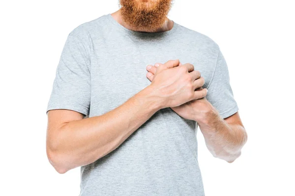 Ausgeschnittene Ansicht eines bärtigen Mannes im grauen T-Shirt, der die Hände am Herzen hält, isoliert auf weiß — Stockfoto