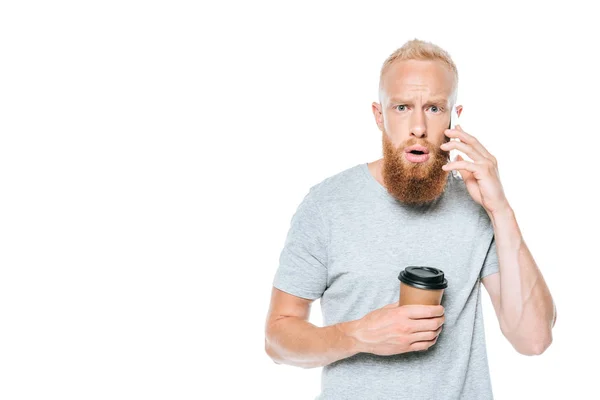 Shocked bearded man with coffee to go talking on smartphone, isolated on white — Stock Photo