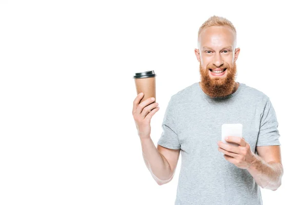 Uomo barbuto sorridente con caffè per andare utilizzando smartphone, isolato su bianco — Foto stock