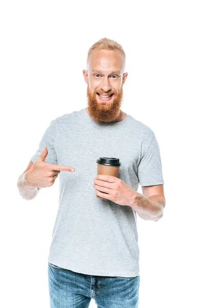 Hombre barbudo sonriente en camiseta apuntando al café para llevar, aislado en blanco - foto de stock