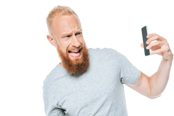 Агресивний чоловік кричить і дивиться на смартфон з порожнім екраном, ізольований на білому — стокове фото