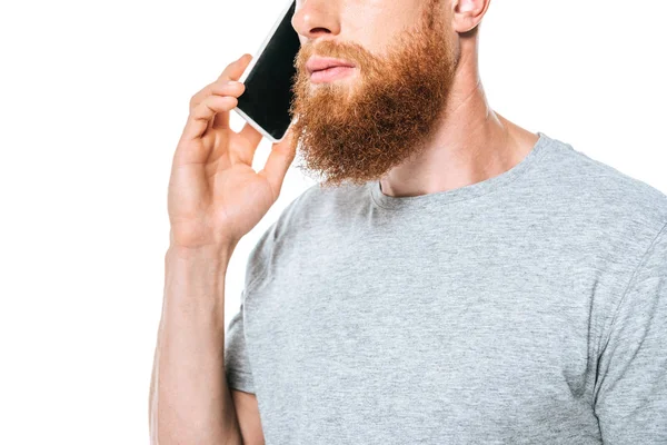 Обрезанный вид серьезного бородатого человека разговаривающего на смартфоне, изолированного на белом — стоковое фото
