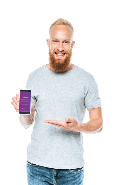 KYIV, UCRANIA - 27 de agosto de 2019: hombre barbudo sonriente que presenta el teléfono inteligente con aplicación instagram, aislado en blanco - foto de stock