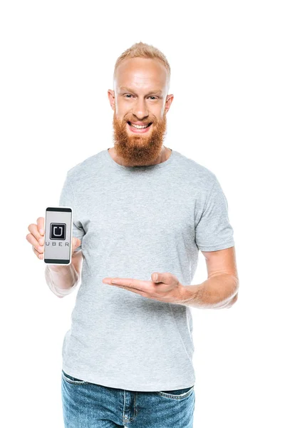 KYIV, UKRAINE - 27 AOÛT 2019 : homme barbu souriant présentant smartphone avec application uber, isolé sur blanc — Photo de stock