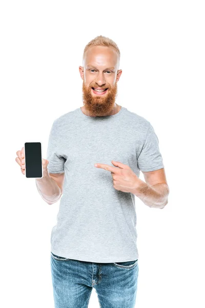 Hombre barbudo apuntando al teléfono inteligente con pantalla en blanco, aislado en blanco - foto de stock