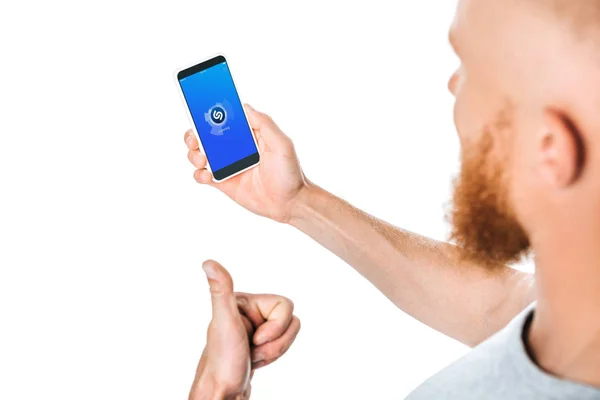 KYIV, UCRAINA - AGOSTO 27, 2019: vista ritagliata dell'uomo che mostra il pollice verso l'alto e guarda lo smartphone con l'app shazam, isolato su bianco — Foto stock