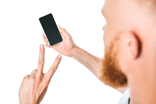 Vue recadrée de l'homme regardant smartphone avec écran blanc et montrant le signe de victoire, isolé sur blanc — Photo de stock