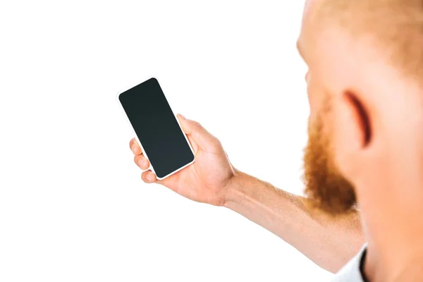 Обрезанный вид человека, смотрящего на смартфон с пустым экраном, изолированный на белом — стоковое фото