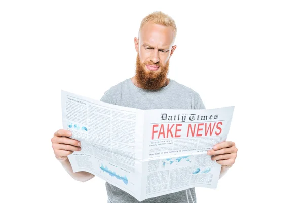 Скептичний бородатий чоловік читає газету з фальшивими новинами, ізольований на білому — стокове фото