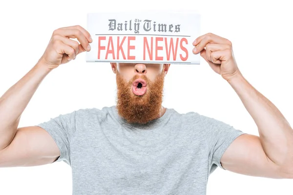 Homem barbudo chocado segurando jornal com notícias falsas na frente dos olhos, isolado em branco — Fotografia de Stock