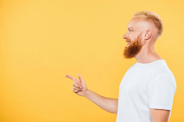 Retrato de perfil de homem barbudo bonito apontando para algo, isolado em amarelo — Fotografia de Stock