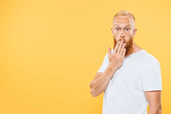 Retrato de homem barbudo surpreso cobrindo boca, isolado em amarelo — Fotografia de Stock