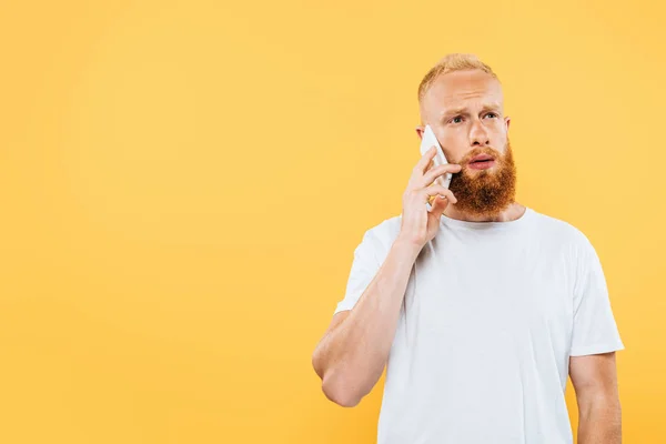 Задумчивый бородатый мужчина разговаривает на смартфоне, изолированный на желтом — стоковое фото