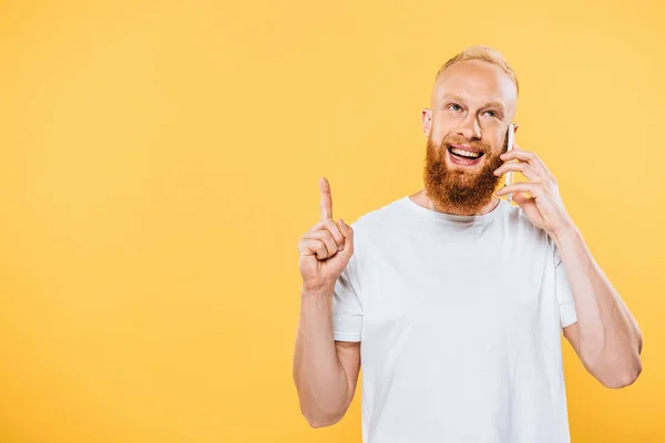 Lächelnder bärtiger Mann, der eine Idee hat, während er auf dem Smartphone spricht, isoliert auf gelb — Stockfoto