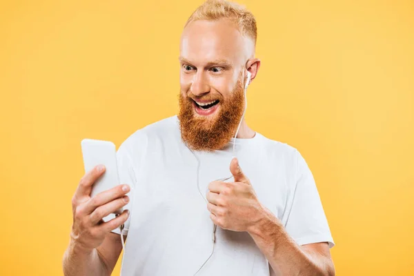 Homme barbu gai avec écouteurs prenant selfie sur smartphone et montrant ok signe, isolé sur jaune — Photo de stock