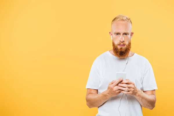 Schöner ernster Mann, der Musik mit Kopfhörern und Smartphone hört, isoliert auf gelb — Stockfoto