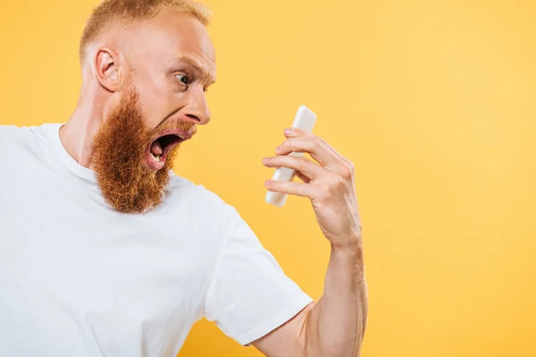 Arrabbiato uomo barbuto urlando allo smartphone, isolato sul giallo — Foto stock