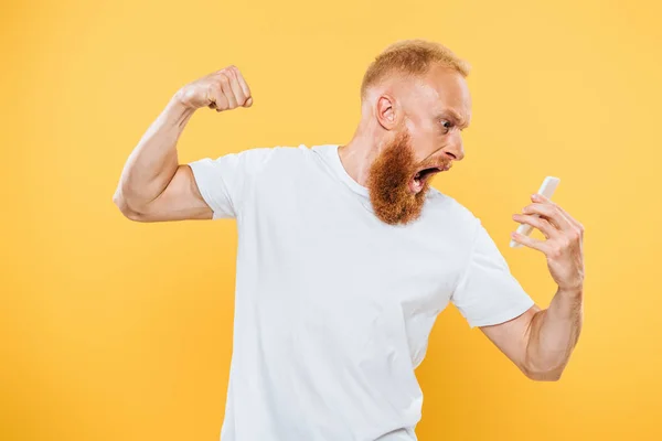 Hombre barbudo agresivo gestos y gritos en el teléfono inteligente, aislado en amarillo - foto de stock