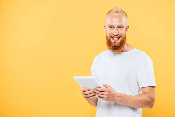 Hombre barbudo feliz usando tableta digital, aislado en amarillo - foto de stock