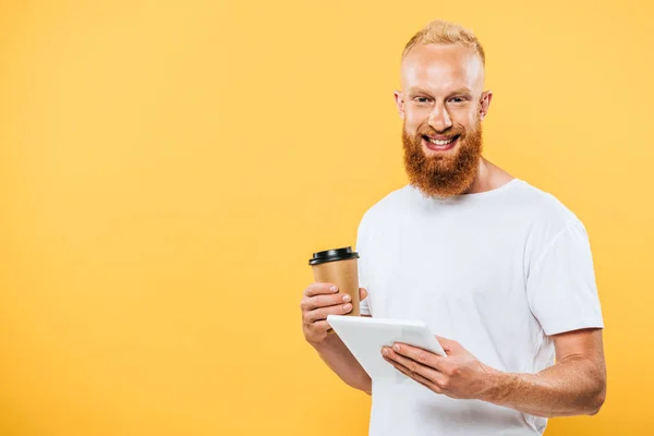 Hombre barbudo sonriente con café para usar tableta digital, aislado en amarillo - foto de stock