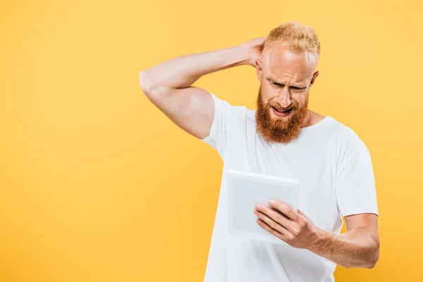 Обеспокоенный бородатый человек с помощью цифровой таблетки, изолированные на желтый — стоковое фото