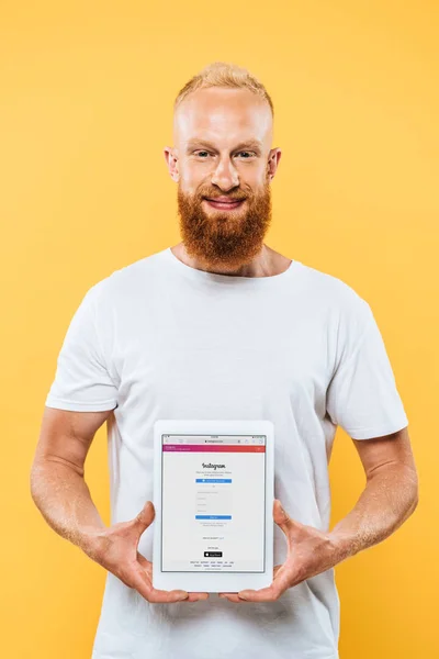 KYIV, UCRANIA - 27 de agosto de 2019: hombre barbudo feliz mostrando tableta digital con aplicación de instagram en la pantalla, aislado en amarillo - foto de stock