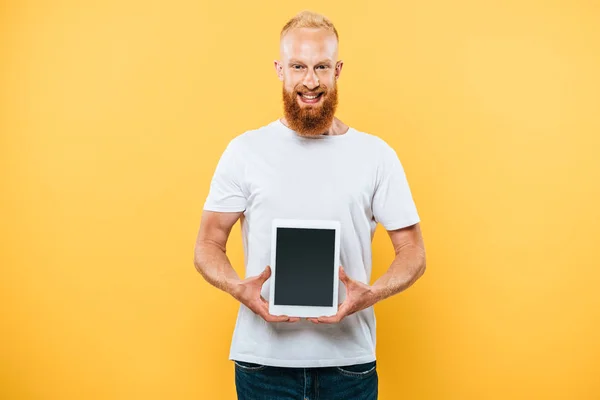 Веселый человек показывает цифровой планшет с чистым экраном, изолированный на желтый — стоковое фото