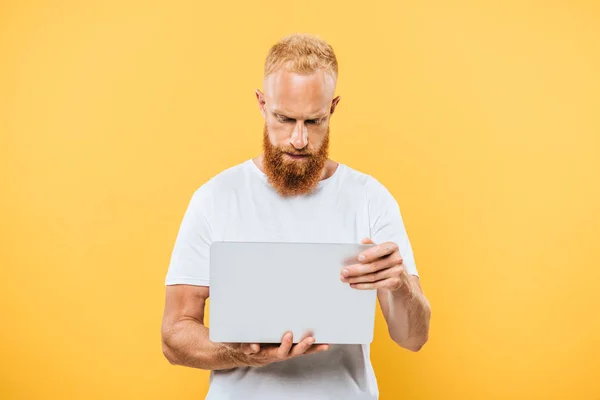 Hombre barbudo reflexivo usando el ordenador portátil, aislado en amarillo - foto de stock