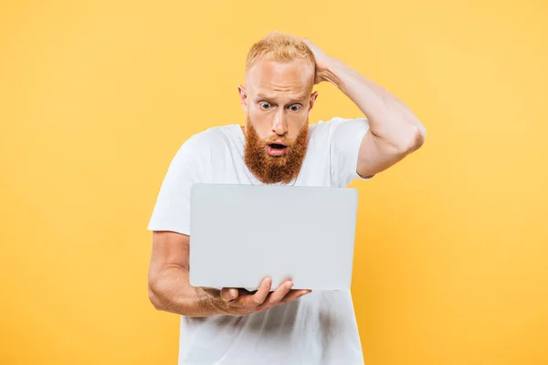 Тривожний бородатий чоловік використовує ноутбук, ізольований на жовтому — стокове фото