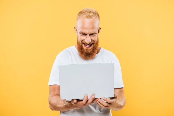 Homme barbu joyeux en utilisant un ordinateur portable, isolé sur jaune — Photo de stock