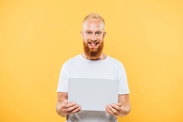 Felice uomo barbuto utilizzando il computer portatile, isolato su giallo — Foto stock