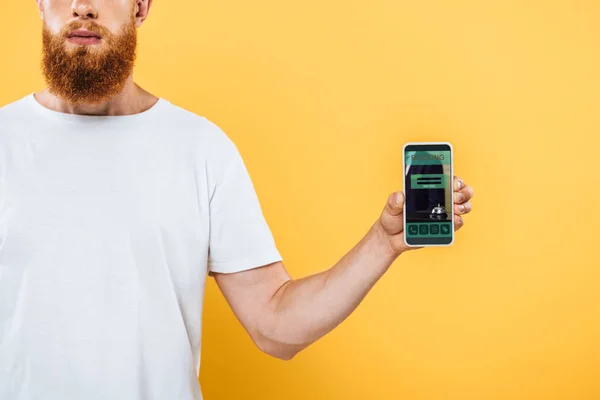 Cropped view of bearded man showing smartphone with booking app, isolated on yellow — Stock Photo